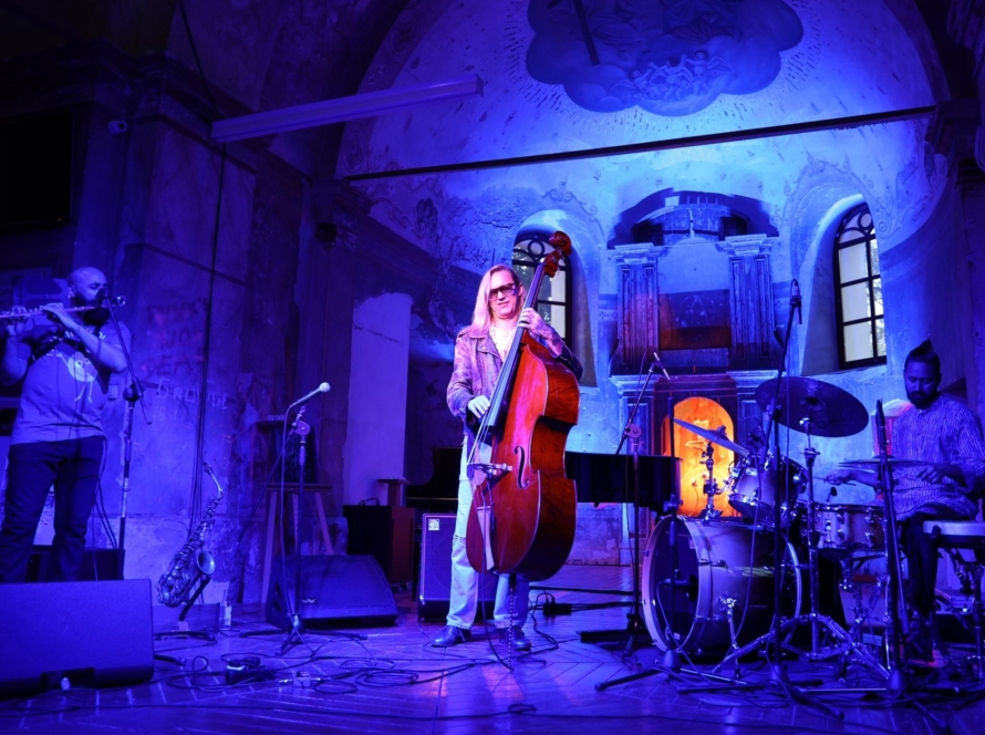 Muzycy grający na scenie w pomieszczeniu oświetlonym na niebiesko